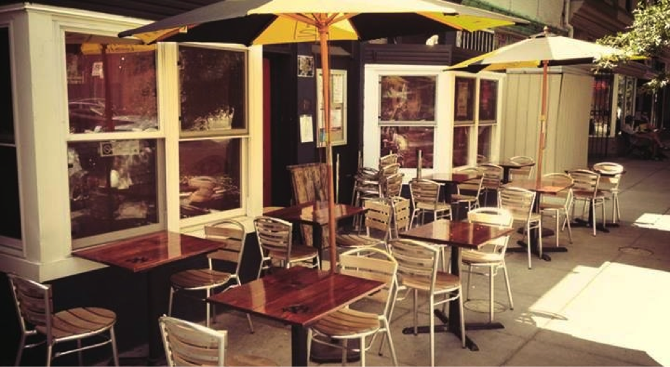 Outdoor sidewalk seating with wooden tables and yellow umbrellas in soft daylight