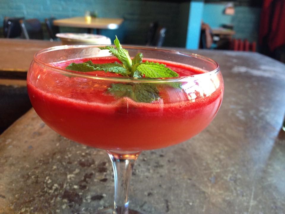 A red cocktail garnished with mint in a coupe glass on a wooden bar